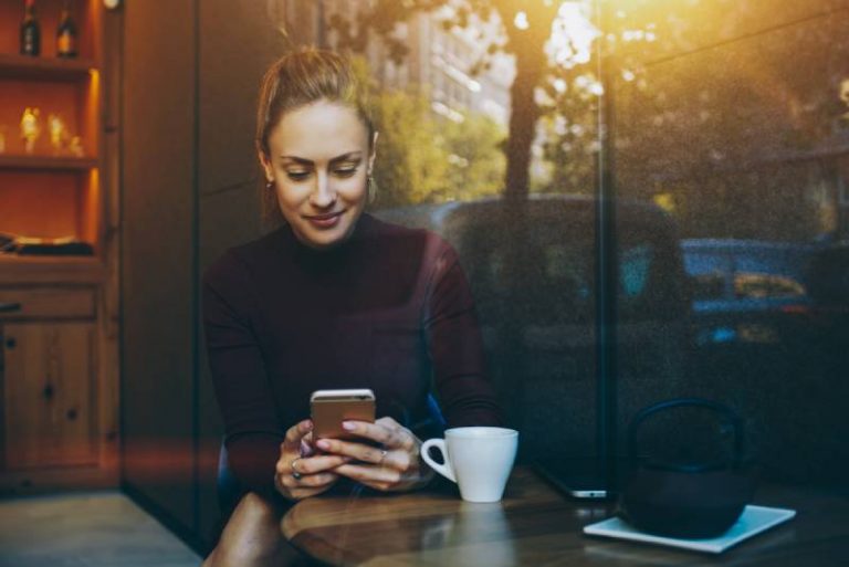 Une smiliwoman envoie des SMS au téléphone dans un café