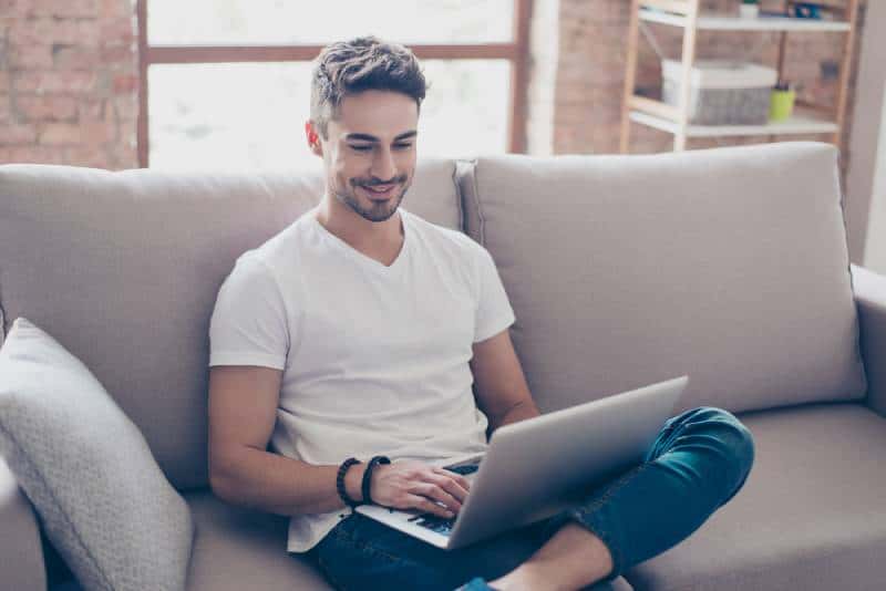 Un homme souriant regarde son ordinateur portable, assis à la maison
