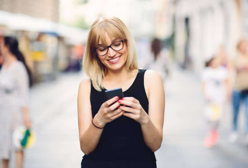 Une belle femme urbaine souriante envoie des SMS sur son smartphone