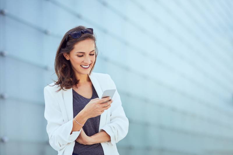 Une belle jeune femme heureuse qui envoie des SMS et sourit dans un cadre extérieur moderne