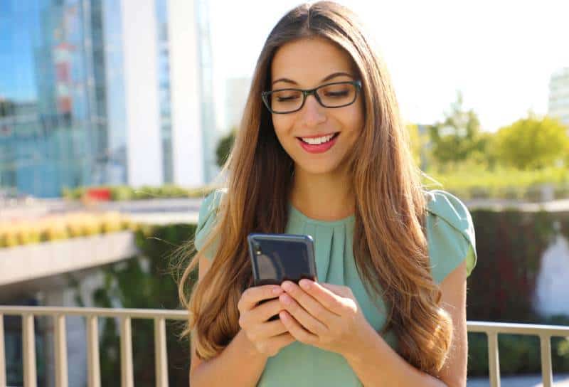 Une femme d'affaires heureuse et souriante avec un téléphone portable dans la rue.