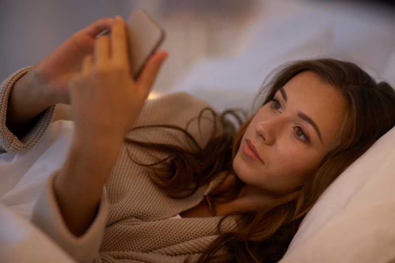 Une femme heureuse qui envoie des SMS sur son smartphone au lit à la maison
