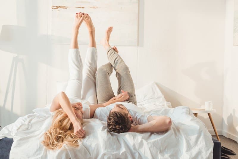 couple heureux couché dans la chambre avec les jambes vers le haut