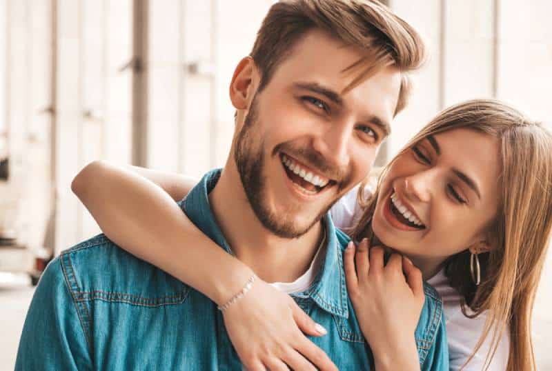 couple souriant tandis que la petite amie l’étreignant par derrière