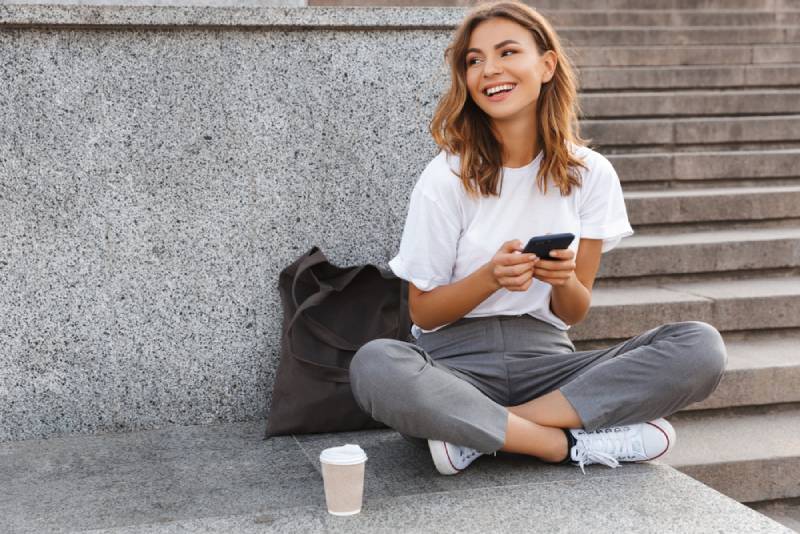 femme assise dans les escaliers de la rue, les jambes croisées et tenant le téléphone