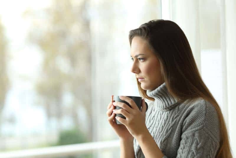 femme pensante tenant une tasse de thé et regardant dehors