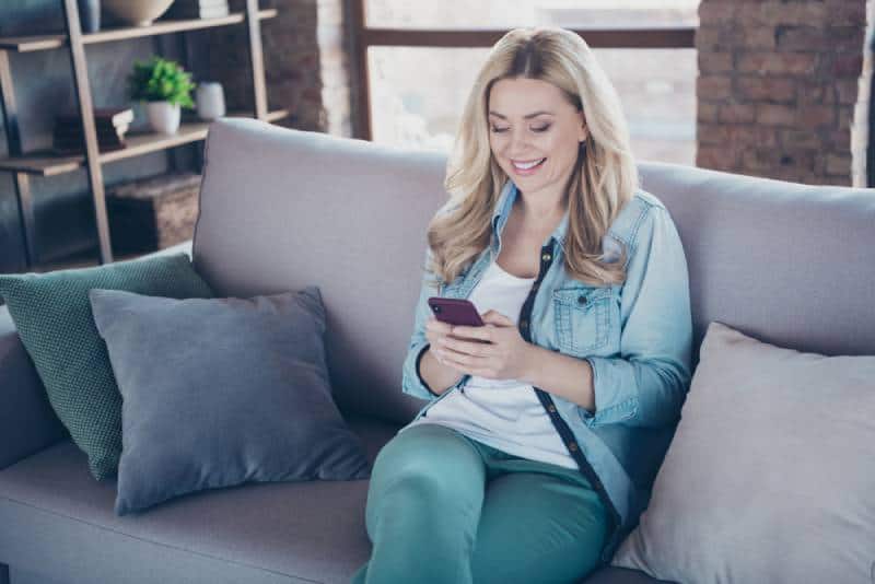 femme souriante séance à divan maison et textos elle téléphone
