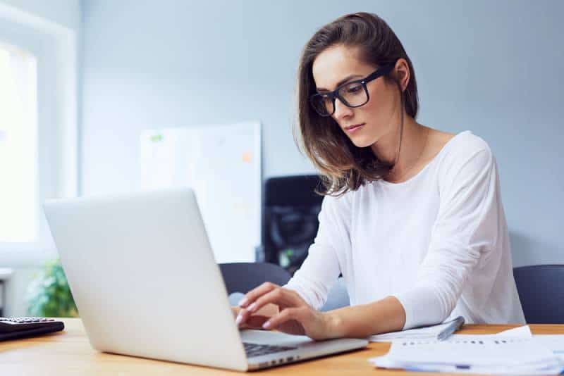 femme s’asseyant au bureau et tapant l’ordinateur portatif