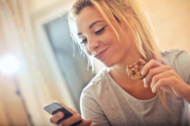 fille textos sur le téléphone tout en mangeant cookie à la maison