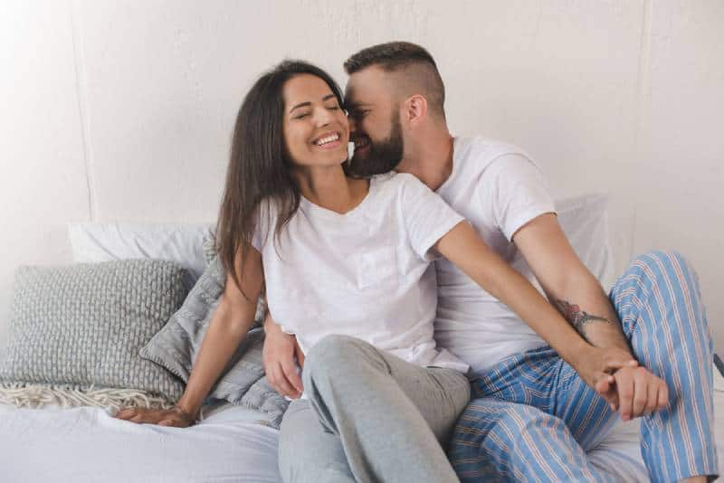 jeune couple souriant et s'embrassant dans son lit à la maison