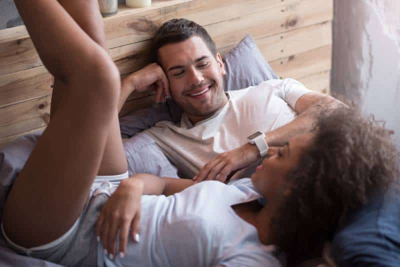 un couple heureux allongé sur le lit et qui parle