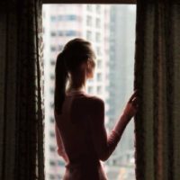 Jeune femme regardant par la fenêtre de son appartement