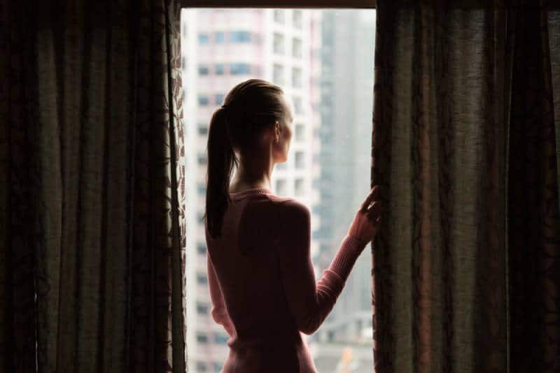 Jeune femme regardant par la fenêtre de son appartement