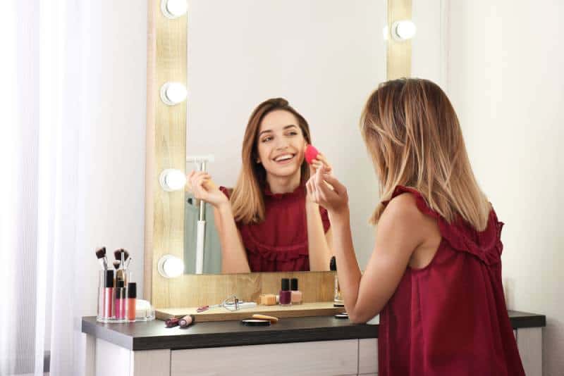 Femme souriante se maquillant devant le miroir