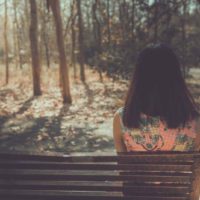 Femme triste assise sur le banc de l'angle du dos dans le parc