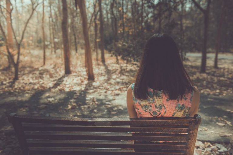 Femme triste assise sur le banc de l'angle du dos dans le parc
