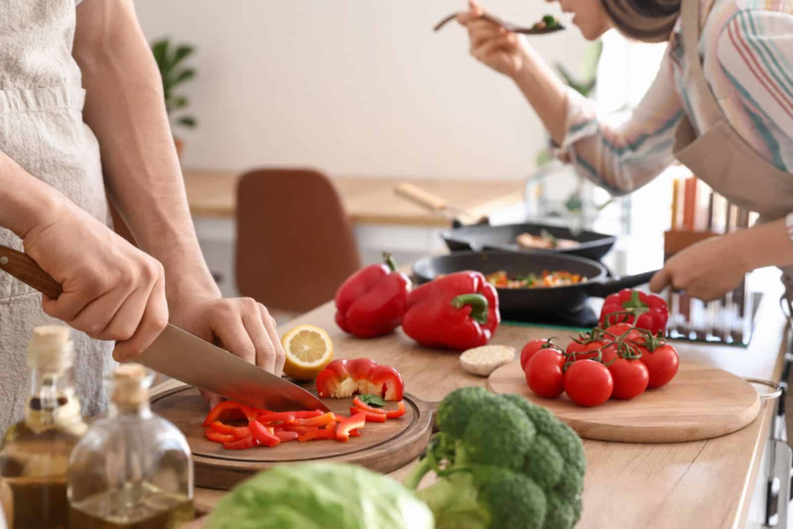 Jeune homme coupant le poivron dans la cuisine pendant qu'une femme dégustait