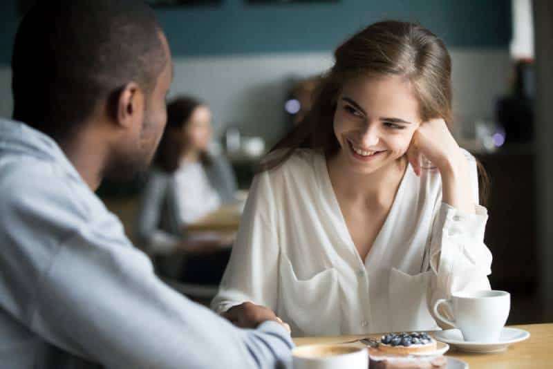 Un couple interracial heureux flirte en parlant assis à la table d'un café