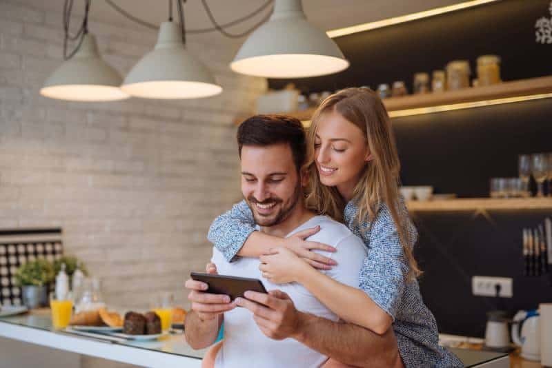 Un couple souriant regarde le téléphone dans la cuisine