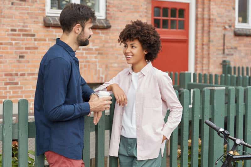 Un jeune couple diversifié se rencontre dans une rue rurale, se tient près d'une clôture verte