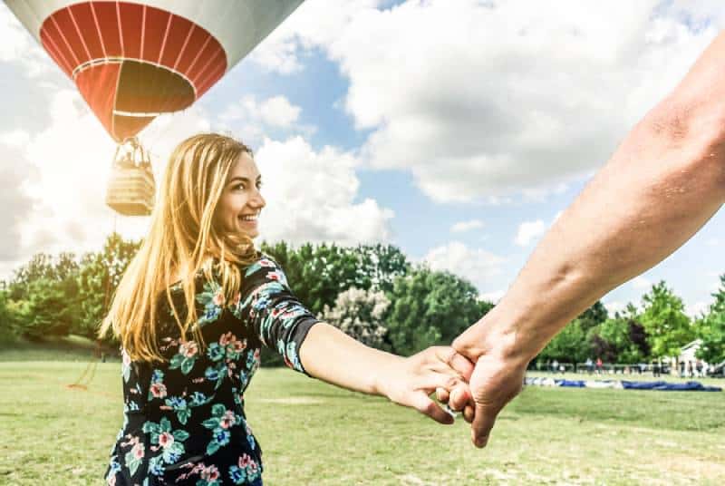 Une jeune femme heureuse veut faire un tour en ballon en tenant la main de son petit ami