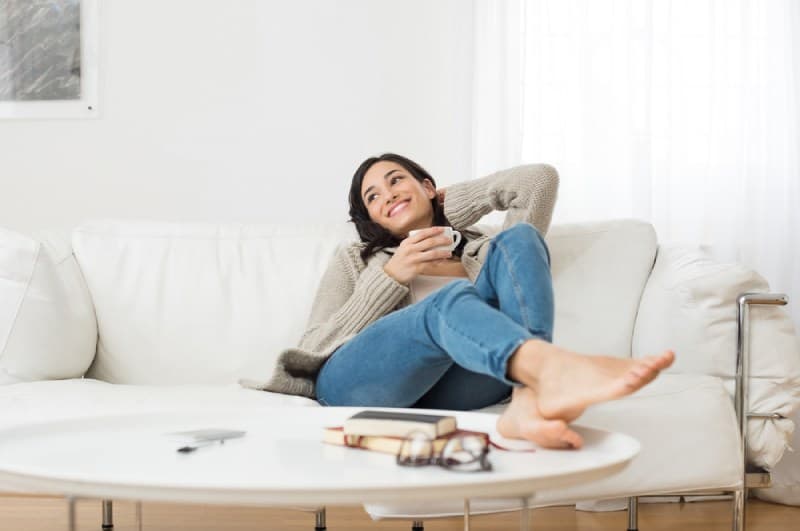 femme souriante assise sur un canapé en buvant du thé