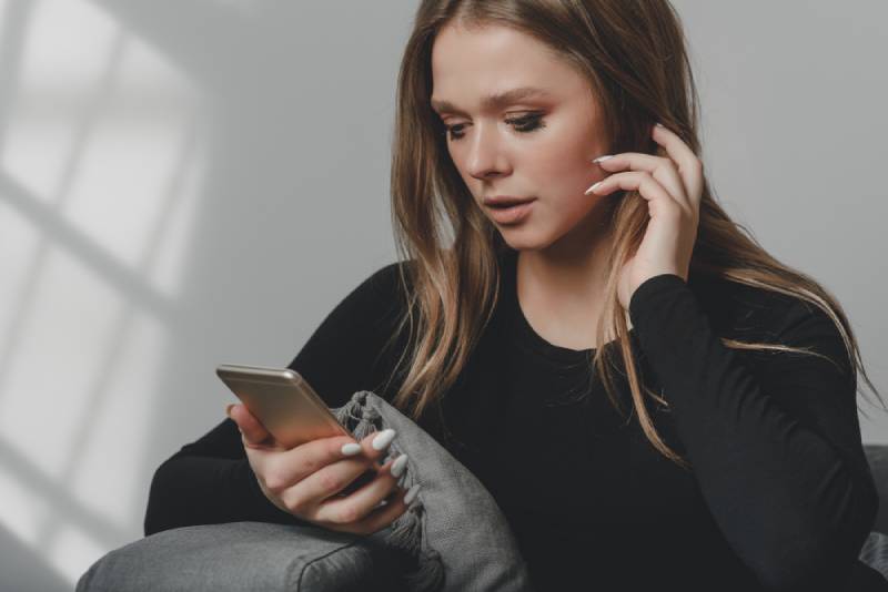 femme à la maison regardant son téléphone de façon confuse