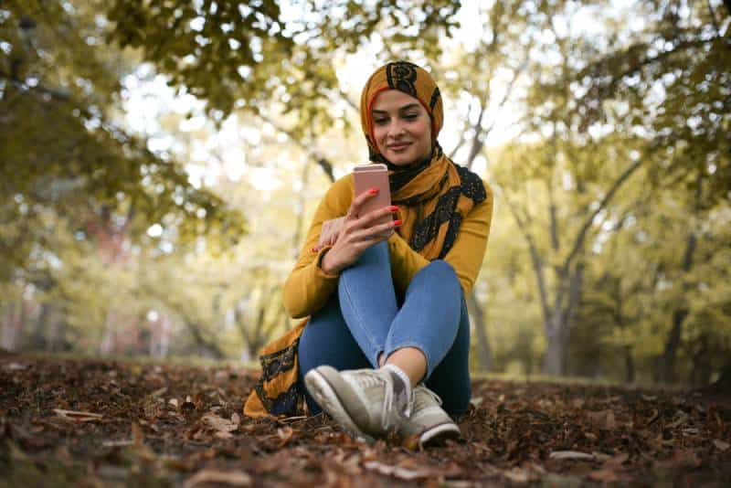 jeune femme heureuse, assise dans la forêt et tapant au téléphone
