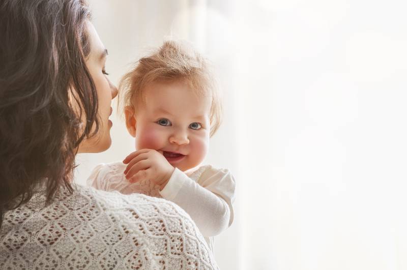 un bébé mignon tient ses doigts dans ses bras
