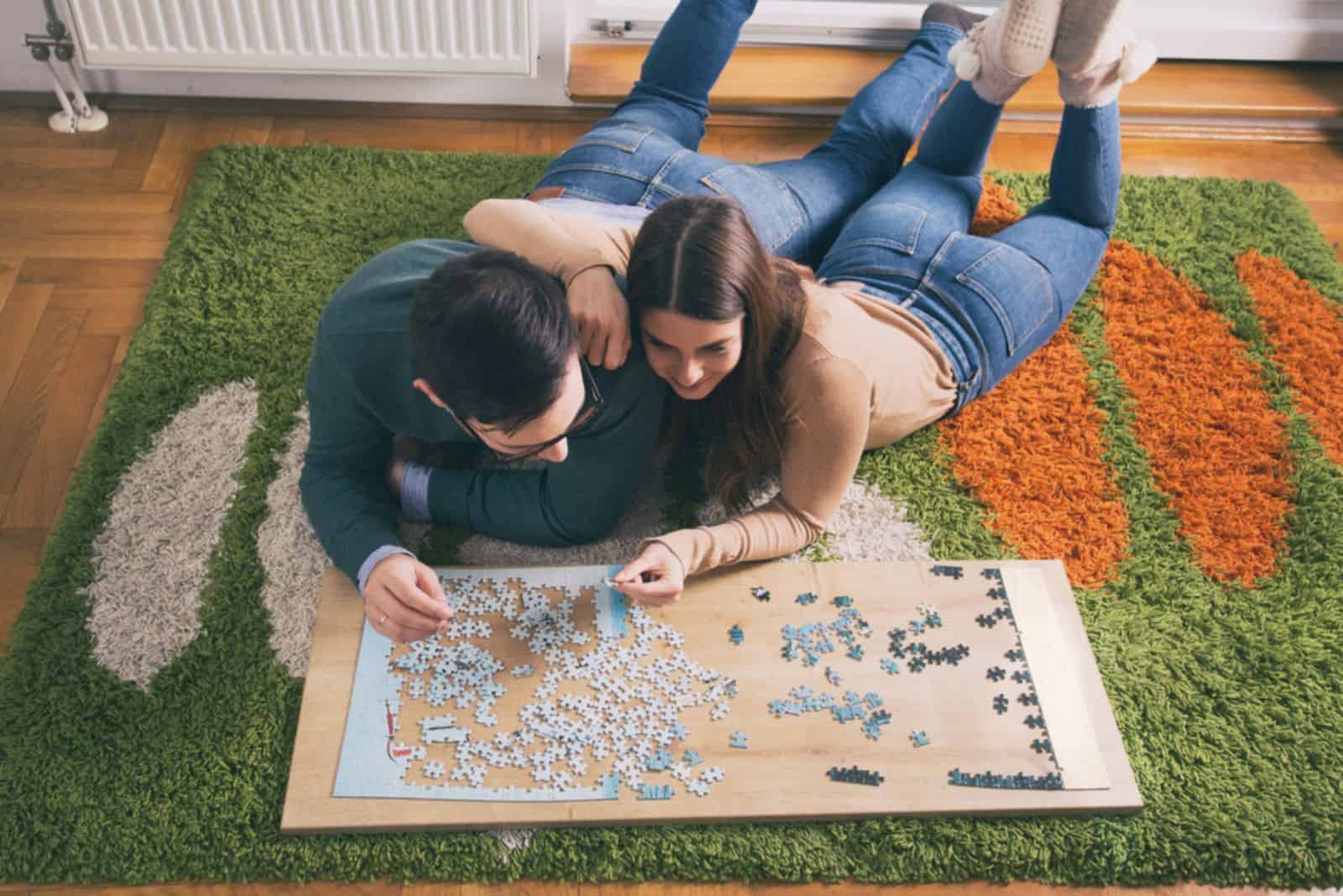 un jeune couple est allongé sur le sol et assemble un puzzle
