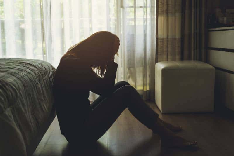 Jeune femme solitaire assise, la tête déprimée dans les mains, dans la chambre sombre
