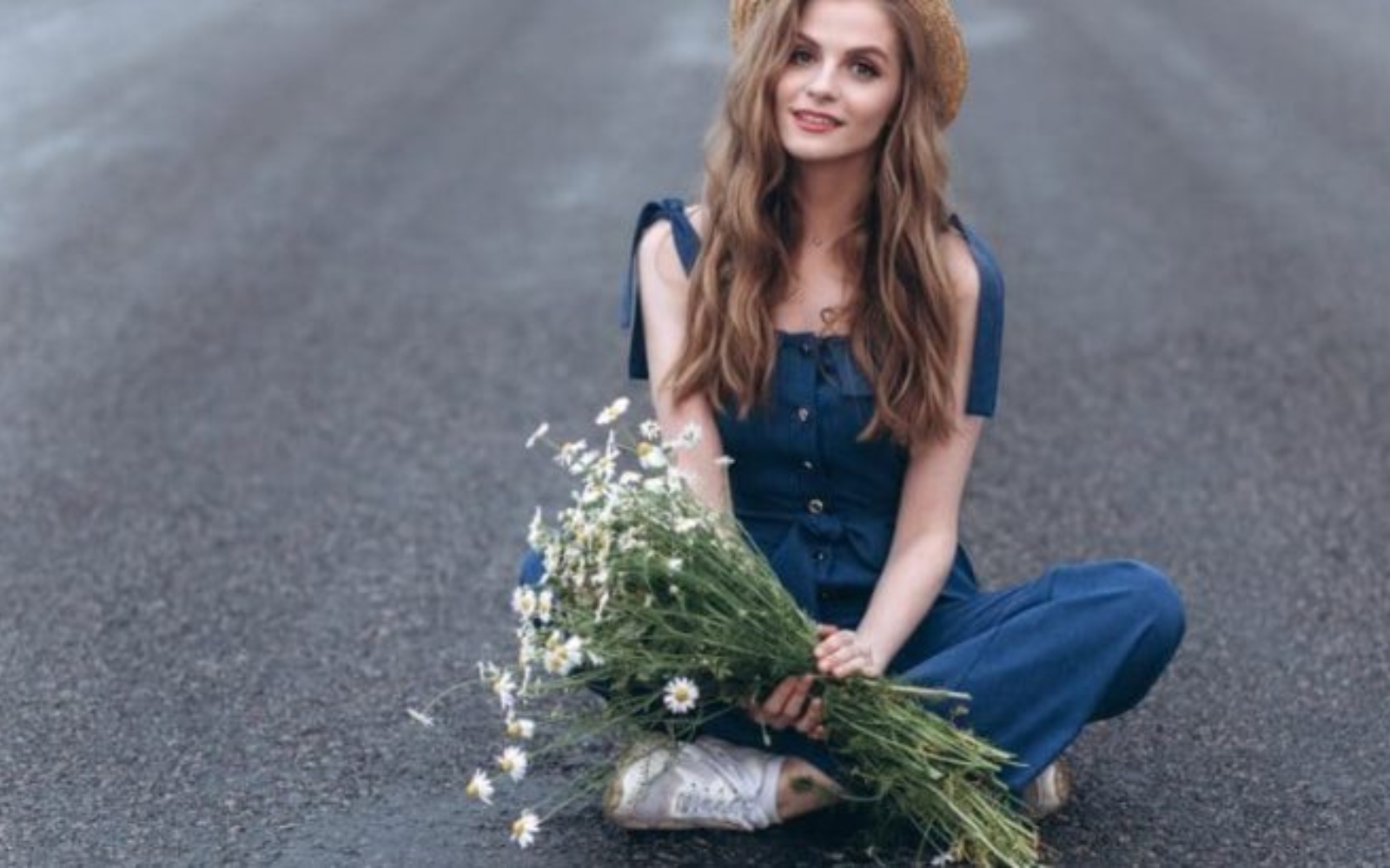 femme tenant une fleur et assise sur une surface en beton