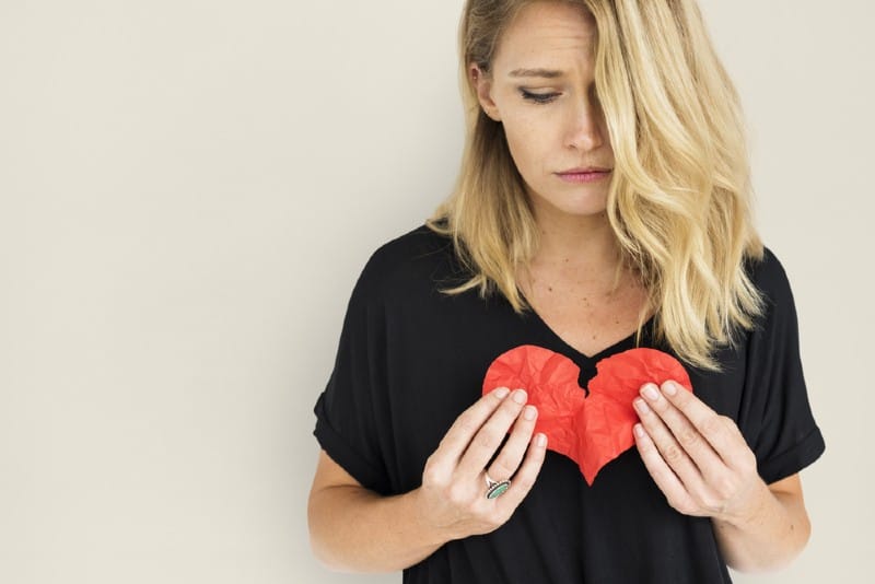 Une femme triste portant une chemise noire tenant un coeur brisé en papier rouge