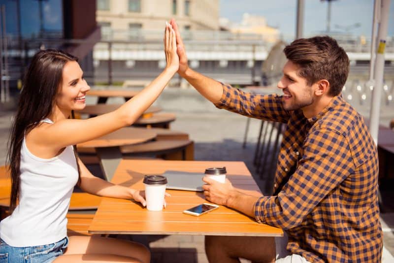 homme et femme assis l'un en face de l'autre près de la table et donnant un high five