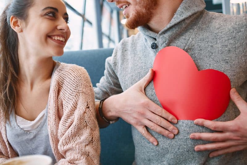 Un homme tenant un coeur rouge devant une femme heureuse