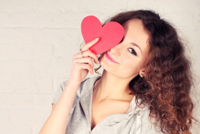 une femme tenant un coeur de papier rouge devant l'un de ses yeux