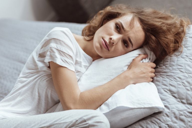femme triste avec sa tête sur un oreiller blanc