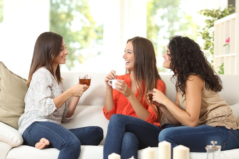 trois jeunes femmes assises sur un canapé, boire du thé et parler