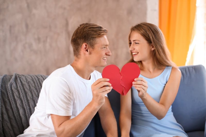 un homme et une femme tenant des moitiés de coeur de papier rouge