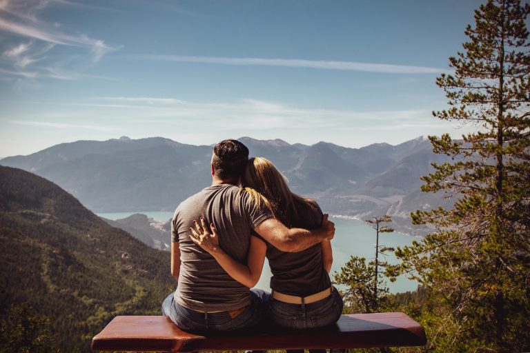 un homme et une femme sont assis sur un banc, embrassant le dos tourné
