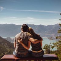 un homme et une femme sont assis sur un banc, embrassant le dos tourné