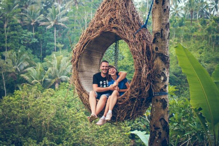 Un homme et une femme souriants sur un hamac brun à côté des arbres