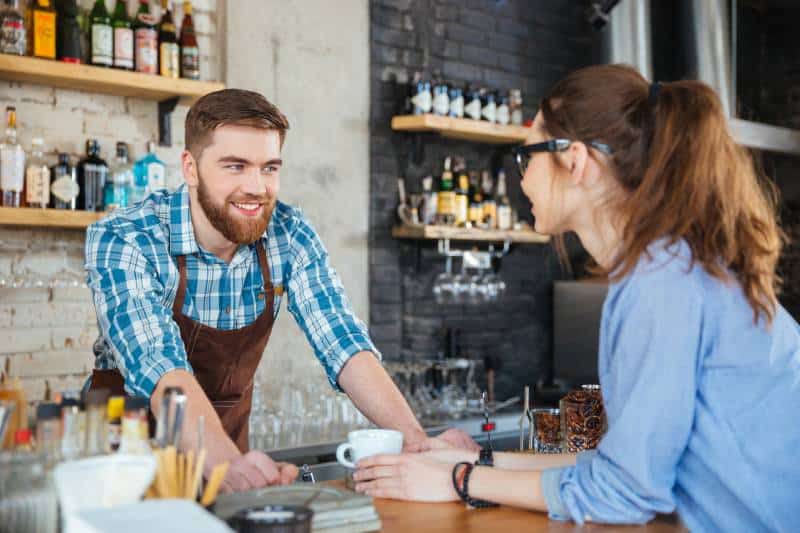 Barista souriante et jeune jolie femme à lunettes discutant dans un café