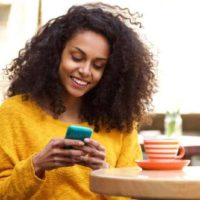 femme afro portant un sweatshirt jaune et tapant sur son téléphone