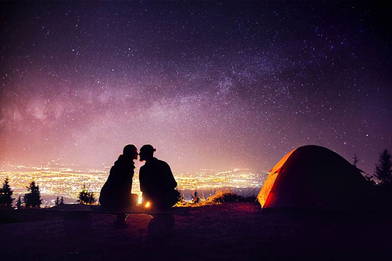 Couple heureux en silhouette s'embrassant près d'un feu de camp et d'une tente orange