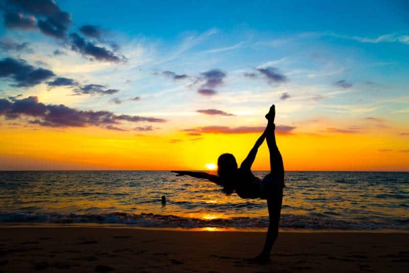 Des sportives en bonne santé font du yoga et de la méditation au coucher du soleil sur la plage
