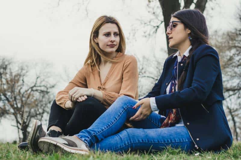 Deux jeunes filles sylvestres assises sur l'herbe et racontant de tristes histoires de vie, dans un parc par une belle journée de printemps