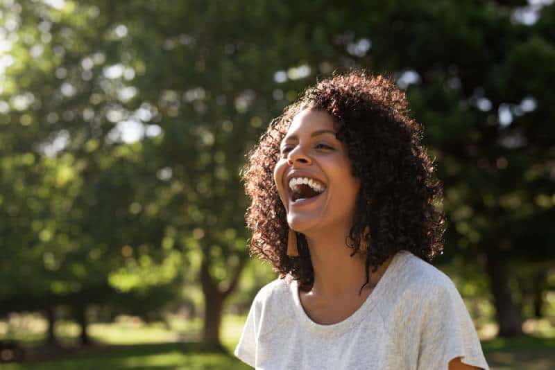 Femme riant avec des cheveux bouclés alors qu'elle se tenait dehors dans un parc