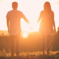 un homme et une femme se tenant la main face au coucher du soleil