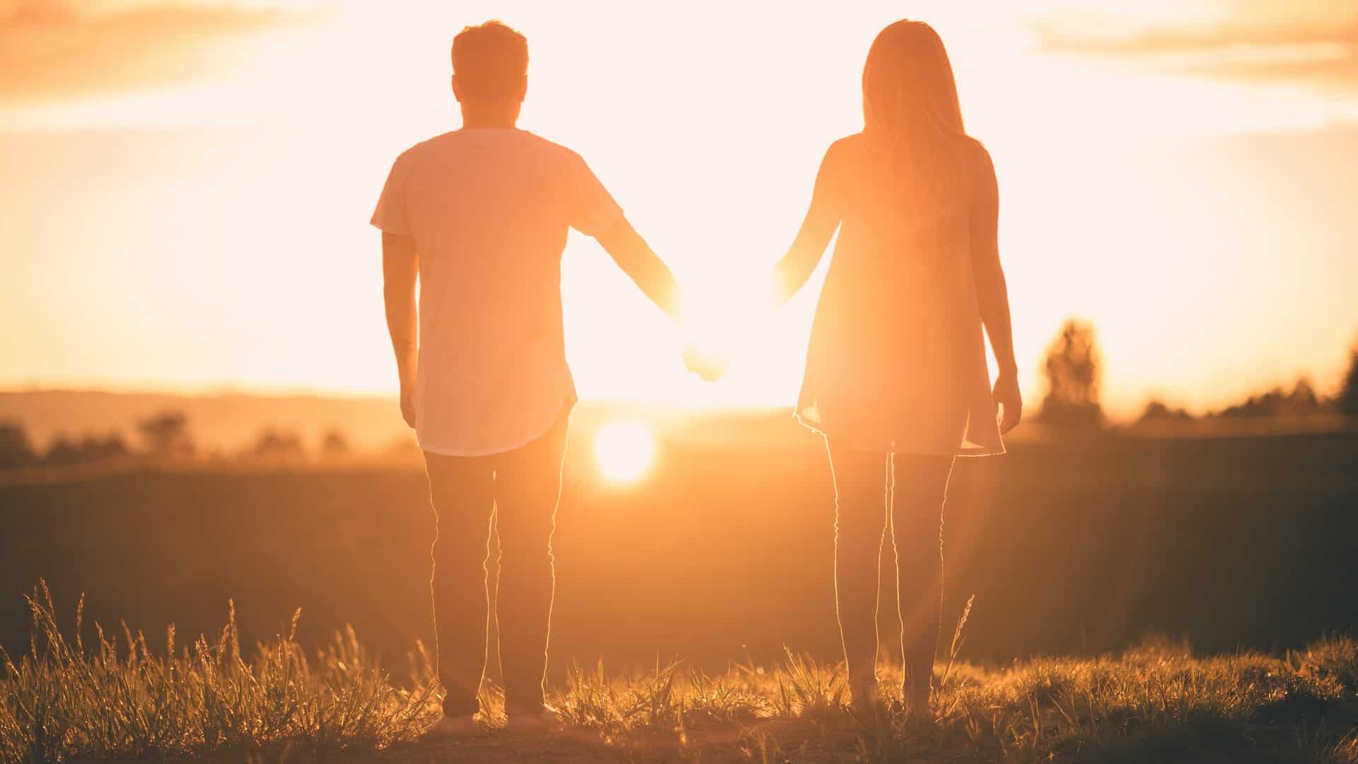 un homme et une femme se tenant la main face au coucher du soleil